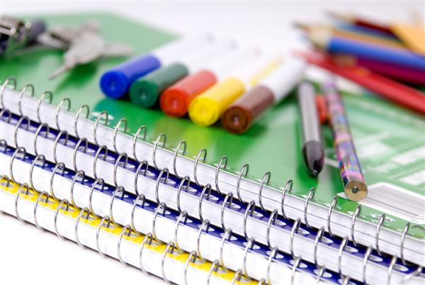 A pile of spiral notebooks with markers and pencils sitting on top. A pile of spiral notebooks with markers and pencils sitting on top.